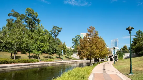 Paved walking path next to canal in The Woodlands, Texas with office buildings in background.